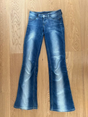Blå utsvängda jeans från Cheap Monday - Snygga blå jeans från Cheap Monday med utsvängda ben och coola slitningar framtill. Klassisk femficksmodell med låg midja och tydliga loggopatchar bak. Perfekta för dig som gillar retrostil och vill sticka ut lite extra.