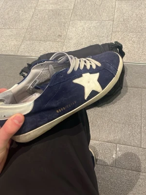Marinblå Golden Goose - Slitna men extremt snygga och sällsynta skor från golden goose. Skicket är inte så värst bra, därav priset. Sulan på höger börjar lossna lite i hälen. Inuti är de använda, men de är äkta iallafall. De är i skick för att användas men skulle rekommendera att försöka fixa hälen inom några månader.