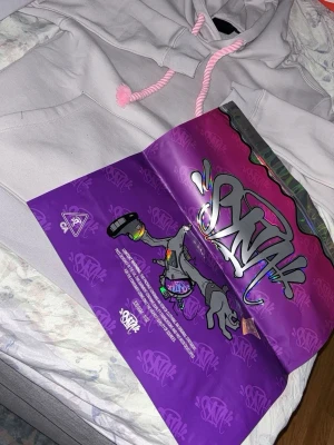 Ljusgrå hoodie från SNTK - Säljer en ljusgrå hoodie från SNTK med feta rosa snören i huvan. Hoodien har klassisk känguruficka framtill och är gjord i mjukt bomullsmaterial. Perfekt för dig som gillar streetwear och vill sticka ut med detaljerna.