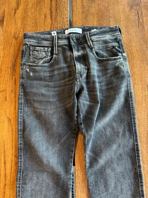 Svarta Replay jeans med slitningar - Snygga svarta jeans från Replay med tvättad look och diskreta slitningar. Klassisk femficksmodell med Replay-logga på myntfickan. Jeansen har raka ben och är tillverkade i denim med en cool, lite sliten finish.