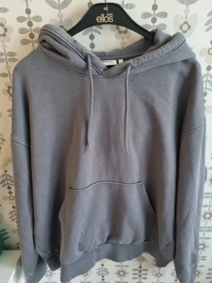 Grå oversized hoodie med huva - Säljer en grå oversized hoodie från Ellos med stor känguruficka framtill och justerbar dragsko i huvan. Hoodien har ribbade muddar vid ärmslut och nederkant, perfekt för en avslappnad och trendig look.