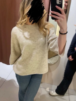 Beige stickad tröja med vida ärmar - Mysig beige stickad tröja med avslappnad passform och vida trekvartsärmar. Tröjan har en enkel rund halsringning och är tillverkad i ett mjukt material som passar perfekt till jeans eller kjol. Tröjan är i storlek S från Gina Tricot. 