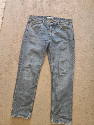 Blå raka jeans i klassisk modell - Säljer ett par blå jeans med rak passform och fem fickor. Jeansen har en klassisk tvättad look och normal midja. Perfekta för en avslappnad stil och passar till det mesta. Materialet är denim i bomull.