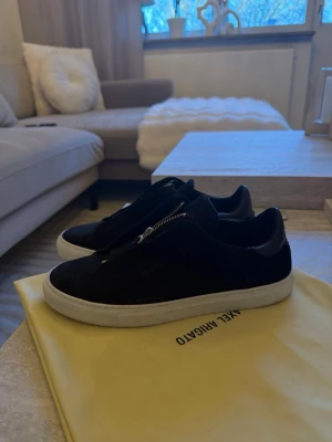 Axel Arigato Half Zip Sneakers – Strl 42 (nästan nya) - Säljer ett par stilrena och eftertraktade sneakers från Axel Arigato Half Zip-modellen i svart mocka med vit sula. En riktigt clean och exklusiv sko som sticker ut lagom mycket tack vare dragkedjan framtill.  Skorna är i mycket fint skick  i princip som nya. Endast testade ute en gång, men tyvärr inte rätt storlek för mig, så de har mest stått.