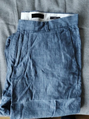 Blå linnebyxor med raka ben - Snygga blå linnebyxor med raka ben och klassisk passform. Byxorna har sidofickor och hällor för skärp. Perfekta för en avslappnad och stilren look. Materialet är lätt och luftigt linne som passar bra till varmare dagar.