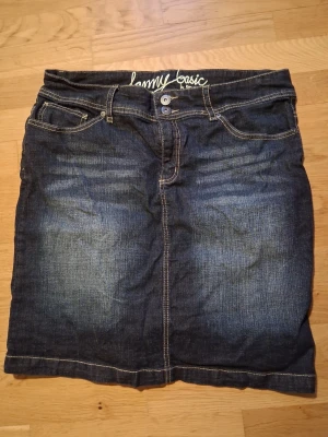 Mörkblå jeanskjol från Lenny Basic - Snygg mörkblå jeanskjol från Lenny Basic med klassisk femficksdesign och kontrastsömmar. Kjolen har knapp- och dragkedjestängning framtill och är tillverkad i slitstarkt denimtyg. Perfekt till vardags för en avslappnad look.