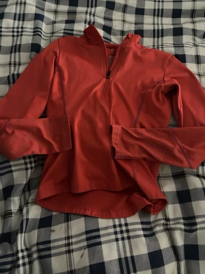 Röd långärmad träningsöverdel SOC - Röd långärmad träningsöverdel från SOC med halv dragkedja framtill och hög krage. Materialet är syntetiskt och designen är slim fit, perfekt för sport och aktivitet. Diskreta detaljer på ärmarna och lätt stretch för ökad rörelsefrihet.