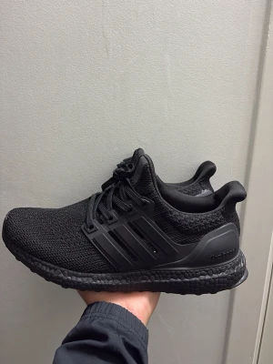 Adidas Ultraboost helsvarta sneakers - Snygga helsvarta Adidas Ultraboost sneakers med stickad ovandel och klassiska tre ränder på sidan. Skorna har en bekväm och responsiv Boost-sula samt svart snörning. Perfekta för dig som gillar stilrena och sportiga skor med modern känsla.
