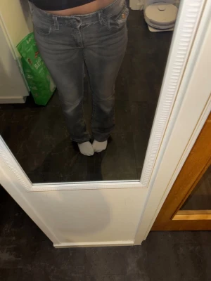 Grå bootcut jeans med slitningar - Säljer ett par grå bootcut jeans med snygga slitningar och klassisk femficksmodell. Jeansen har låg midja och dragkedja med knapp framtill. Perfekta för dig som gillar en avslappnad och trendig stil.