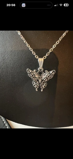 Silverfärgat halsband med fjärilshänge - Snyggt halsband i silverfärg med ett detaljerat fjärilshänge. Kedjan är tunn och har en klassisk länkdesign medan hänget har ett öppet, filigranliknande mönster som ger en unik och trendig look. Perfekt för dig som gillar smycken med naturinspirerade motiv.