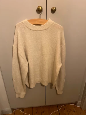 Vit oversized stickad tröja - Enkel och stilren vit stickad tröja med oversized passform och rund halsringning. Tröjan har långa ärmar och ribbade muddar vid ärmslut och nederkant. Perfekt för lager-på-lager och en avslappnad look.