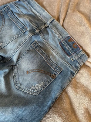Blåa dondup George jeans - Snygga blå jeans från dondup med raka ben och slitna detaljer på bakfickan och framsidan. Klassisk femficksmodell med orangea sömmar och normalhög midja. Perfekta för en avslappnad och trendig look. Waist 34 men passar typ w31
