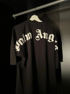 Svart Palm Angels t-shirt med tryck - Svart oversized t-shirt från Palm Angels med stort vitt logotyptryck över ryggen och mindre tryck i nacken. T-shirten har en loose passform och är tillverkad i bomull. Perfekt för en streetwear-look.