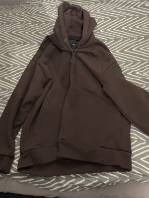 Brun oversized hoodie - Mörkbrun hoodie i oversized modell med stor huva och känguruficka framtill. Tillverkad i mjukt bomullsmaterial och har ribbade muddar vid ärmslut och nederkant. Perfekt för en chill och avslappnad stil.