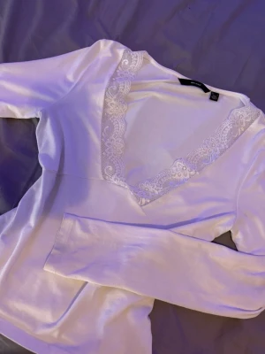Vit långärmad topp med spets - Säljer en vit långärmad topp från Bikbok med djup v-ringning och fina spetsdetaljer runt halsen. Toppen har en mjuk och stretchig känsla, perfekt för att lyfta vilken outfit som helst. Enkel men ändå elegant design. Knappt använd
