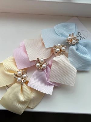 Pastellfärgade rosett hårspännen - Fyra hårspännen i pastellfärger: ljusblå, ljusgul, ljusrosa och creme. Varje spänne har en stor rosett i ribbat tyg och dekoreras med pärlor och små glittriga stenar i mitten. Perfekt för att ge en söt och elegant touch till frisyren.