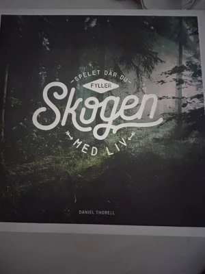 Brädspelet Skogen av Daniel Thorell - En bok med spelinslag där du utforskar och fyller den svenska skogen med liv. Boken har ett mörkt omslag med skogsmotiv och innehåller illustrationer av djur, växter och svampar. Perfekt för dig som gillar natur och biologisk mångfald.Aldrig använt.helt nytt spel.