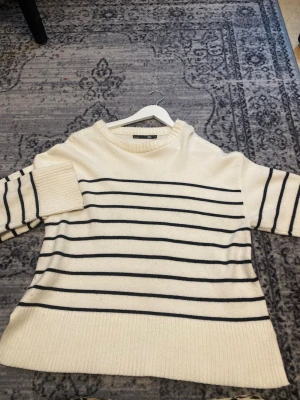 Vit stickad tröja med marinblå ränder - Säljer en krämvit stickad tröja med marinblå horisontella ränder. Tröjan har rund halsringning, långa ärmar och bred ribbstickad kant nedtill och vid ärmsluten. Perfekt för en avslappnad och stilren look.