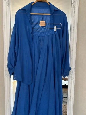 Blått set med skjorta och kjol i batist - Snyggt blått set med en luftig skjorta och matchande lång kjol i tunt, mjukt tyg. Skjortan har klassisk krage och långa ärmar, kjolen har resår i midjan för skön passform. Perfekt för dig som gillar en avslappnad men stilren look. Onesize S M L