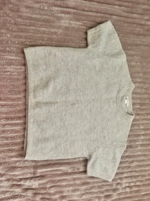 Beige stickad kortärmad topp - En enkel och stilren beige stickad topp med korta ärmar och rund hals. Perfekt att matcha med jeans eller kjol för en clean look. Mjuk och skön kvalitet som känns lyxig mot huden.