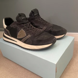 Svarta Philippe Model sneakers - Snygga svarta sneakers från Philippe Model med beige detaljer och vit sula. Skorna har en klassisk låg silhuett, mocka- och textilpaneler samt logotyp på sidan. Perfekta för dig som gillar stilrena och trendiga sneakers.