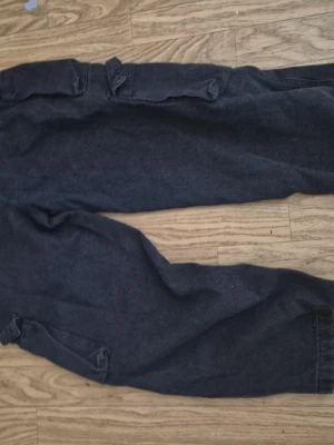 Svarta cargobyxor med fickor - Säljer ett par svarta cargobyxor med klassiska stora sidofickor och rak passform. Byxorna har en avslappnad look och är perfekta för dig som gillar streetwear. Materialet känns slitstarkt och de har en enkel design utan synligt märke.