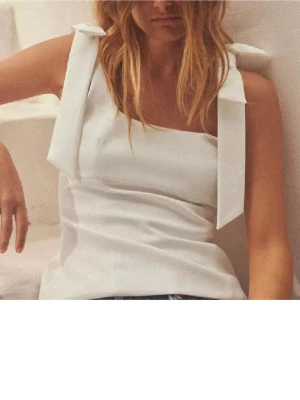 Vit linnetopp med rosetter - Stilren vit linnetopp med breda axelband som knyts i stora rosetter. Använd endast en gång, finns inte längre kvar på hemsidan.