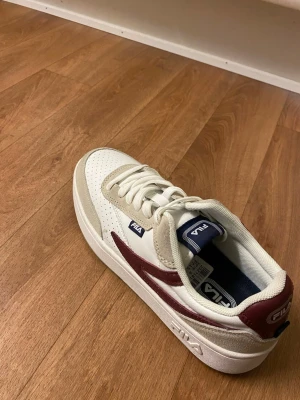 Vita och vinröda sneakers från FILA - Säljer en jätte fin och skön fila skor🤩 De har storlek 38 och funkar för både tjejer och killar. Passar för sommaren och för vintern också. Jätte fin och olika färger. Säljer den för jag behöver för moped 🏍️ priset kan diskuter och hör av er gärna 👍 jag skickar de snabbt och direkt.