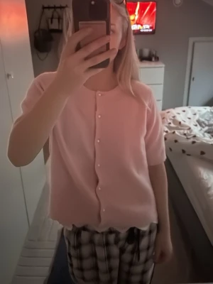 Ljusrosa kofta med pärlknappar - Söt ljusrosa kofta från H&M med korta ärmar och rund halsringning. Koftan har dekorativa pärlknappar framtill och är stickad i ett mjukt material. Perfekt för att addera en gullig touch till din outfit.