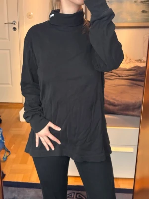 Svart polotröja från Puma 🖤 - Svart långärmad polotröja från Puma med vit broderad logga på kragen. Tröjan är i mjukt material och har en avslappnad passform, perfekt för en chill och stilren look.