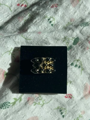 Guldfärgad chunky ring med nitar - Cool statementring i guldfärgad metall med flera upphöjda nitar i både guld och silver. Ringen har en bred, chunky design som verkligen drar blickarna till sig. Perfekt för dig som gillar att sticka ut och vill ha en edgy accessoar till din stil.