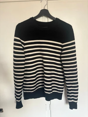 Svartvit randig stickad tröja - Snygg stickad tröja med svarta och vita horisontella ränder. Tröjan har rund halsringning, långa ärmar och ribbade muddar vid ärmslut och nederkant. Perfekt för en stilren och avslappnad look.