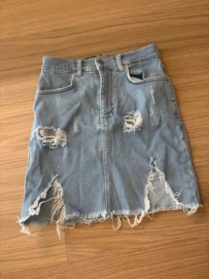 Blå jeanskjol med slitningar - Säljer en blå jeanskjol med råa slitningar och fransig nederkant. .