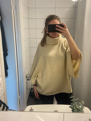 Beige stickad poncho från Zara - Säljer en oversized beige stickad poncho från Zara med polokrage och vida trekvartsärmar. Mjuk och skön kvalitet, perfekt för lager på lager. Passar dig som gillar en avslappnad och trendig stil.