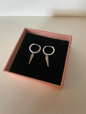 Silver örhängen - Säljer ett par silvriga örhängen i hoop-modell med spetsiga, konformade hängen. Örhängena har en stilren och edgy design, perfekta för att lyfta vilken outfit som helst. 