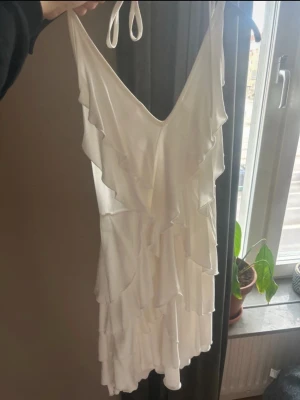 Student/avslutningsklänning - Jättefin vit sommarklänning med halter perfekt till student eller avslutning. Bara använd en gång och i jättebra skick. Går att knyta i nacken och där bak för att göra mindre/större