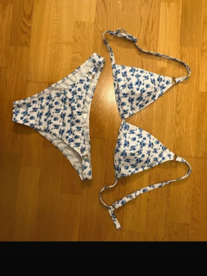Vit och blå blommig bikini - Söt trekantsbikini med vit botten och blått blommönster. Överdelen har knyt i nacken och ryggen, och underdelen har en klassisk midja. Perfekt för stranden eller poolen. Materialet känns mjukt och stretchigt. Både e L men skulle säga lite liten i storleken❤️❤️