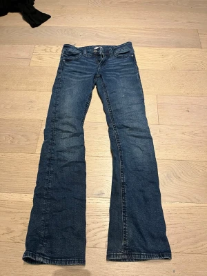 Mörkblå bootcut jeans - Säljer ett par mörkblå bootcut jeans med klassisk femficksdesign och låg midja. Jeansen har en lätt tvättad look och är tillverkade i denim med lite stretch för skön passform. Perfekta för dig som gillar retrovibbar och vill ha ett par jeans som sticker ut.