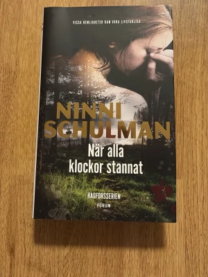När alla klockor stannat av Ninni Schulman - Spännande kriminalroman av Ninni Schulman från Hagforsserien. Omslaget är mörkt med skogsmotiv och en kvinna i bakgrunden. Boken är tryckt på vanligt papper och har en hård pärm. Perfekt för dig som gillar deckare med vardagsnära miljöer och starka karaktärer.