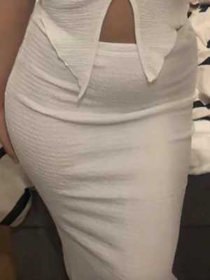 Vit kjol set - Säljer en vit långkjol med figurnära passform och snygg struktur i tyget. Kjolen har en enkel och stilren design som passar perfekt till crop tops eller instoppade tröjor. Materialet känns mjukt och följsamt. Aldrig använd. Strechigt tyg så passar upp till S. 