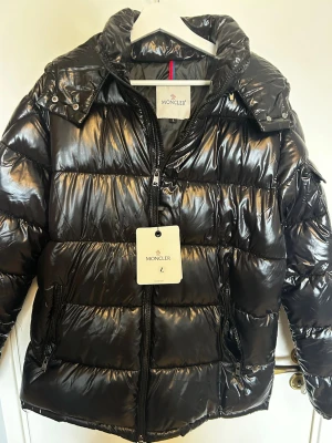 Svart glansig dunjacka från Moncler - Säljer en svart, glansig dunjacka från Moncler med huva och dragkedja framtill. Jackan har två sidofickor med dragkedja. Perfekt för kalla vinterdagar och riktigt snygg streetstil. Pris kan diskuteras😃🤝