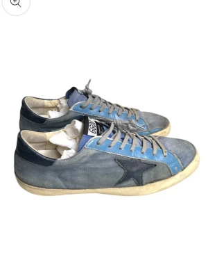 Blå GGDB sneakers med stjärndetalj - Snygga sneakers från Golden Goose i blått och grått med ikonisk svart stjärna på sidan. Skorna har grå snörning, beige sula och detaljer i mocka och canvas. Perfekta för dig som gillar en avslappnad och trendig stil.