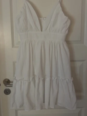 Vit kort sommarklänning med volanger - Säljer en vit klänning från PrettyLittleThing med smala axelband och dragkedja i ryggen, prislappen är kvar. Perfekt inför sommaren💗💗