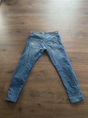 Dondup jeans - Säljer ett par klassiska blå jeans med rak passform och fem fickor. Jeansen har normal midja och subtila slitningar framtill för en avslappnad look. Tillverkade i denim med knappgylf och bälteshällor. Perfekta för en casual stil.