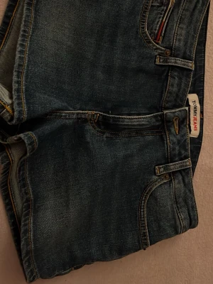 Blå jeansshorts från Tommy Jeans - Snygga blå jeansshorts från Tommy Jeans med klassisk femficksdesign, bälteshällor och logga på bakfickan. Shortsen har en normal passform och är tillverkade i bomull med slitna detaljer för en avslappnad look.