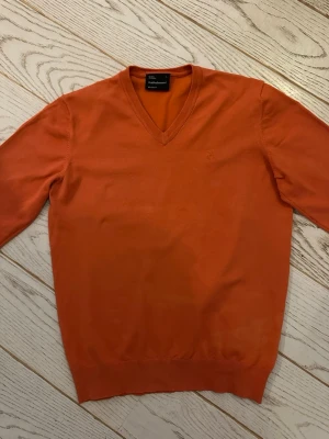 Orange V-ringad tröja Peak Performance  - Snygg orange tröja från Peak Performance med V-ringning och långa ärmar. Tillverkad i mjukt material och har ribbade muddar vid ärmslut och nederkant. Perfekt för dig som vill ha en färgstark och stilren look.