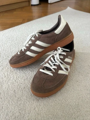 Adidas Spezial bruna sneakers - Bruna Adidas Spezial sneakers i mocka med vita detaljer och klassiska tre ränder på sidan. Skorna har vita skosnören men man får även med bruna skosnören! 