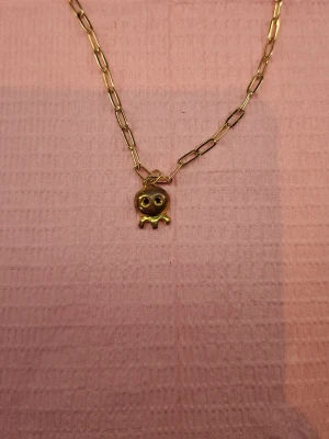 Guldigt halsband med spökhänge/bläckfisk  - Snyggt halsband i guldfärgad metall med ett unikt spökhänge/bläckfisk. Kedjan har större länkar och justerbar längd med karbinlås. Perfekt för dig som gillar lekfulla och trendiga accessoarer.