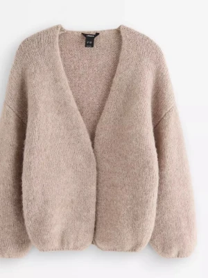 Beige stickad kofta från Lindex - Mjuk och fluffig beige stickad kofta från Lindex med djup v-ringning och långa ärmar. Koftan har en avslappnad passform och är tillverkad i ett mohair-liknande material som känns riktigt cozy. Perfekt att slänga på sig när det är kyligt ute.