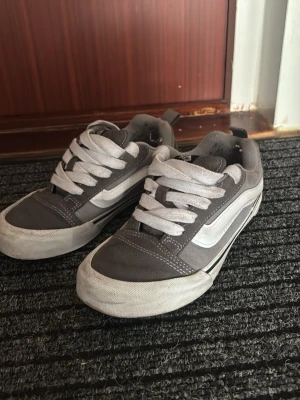 Gråa Vans Old Skool sneakers - Säljer ett par gråa Vans Old Skool sneakers med vit sula och den klassiska vita sidan. Skorna har låga skaft, vita snören och är tillverkade i mocka och textil. Perfekta för en avslappnad streetwear-look. Använda en vår och inte mer än så